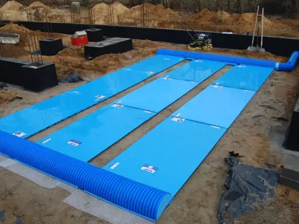 GWC rurowy o dużej długości rozłożony na budowie. Niebieskie płyty izolacyjne i rury tworzą system wentylacji.