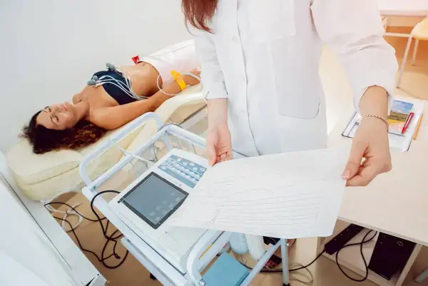 Une patiente allongée, connectée à un électrocardiogramme, pendant que le médecin examine le tracé. Voici comment se passe un électrocardiogramme.
