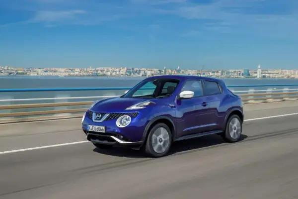 En blå Nissan Juke kör på en bro med en stad i bakgrunden. En perfekt bild för ett nissan juke test.
