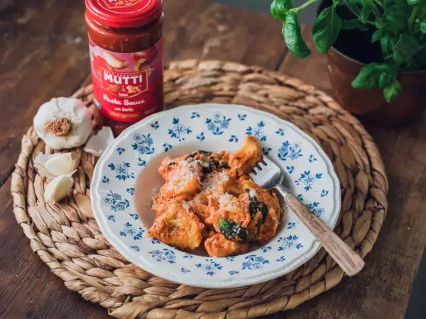 En tallrik med pasta i krämig tomatsås, toppad med parmesan. Bredvid står en burk Mutti pastasås och färsk vitlök. En perfekt italiensk meny fest!