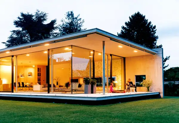 Ein moderner Bungalow mit Glasfronten und einem flachen Dach. Eine Familie entspannt sich auf der Terrasse.