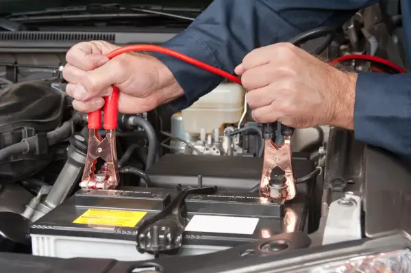 Ręce mechanika podłączają kable rozruchowe do akumulatora samochodowego, rozpoczynając czas ładowania akumulatora.