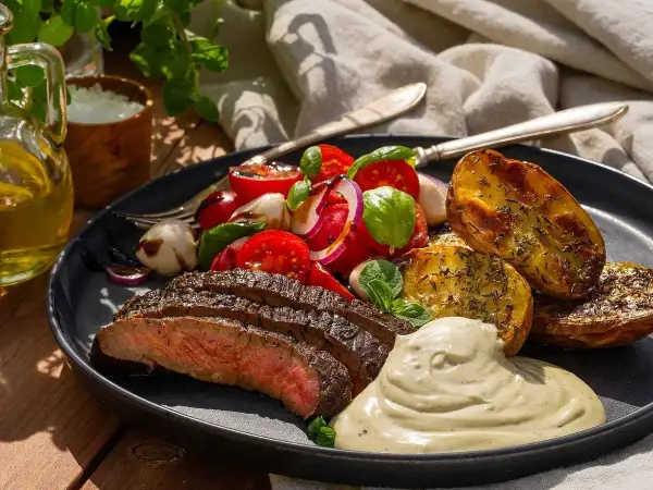 Skivad flankstek med marinad, rostade potatisklyftor, tomatsallad och krämig sås. En perfekt sommarmåltid.