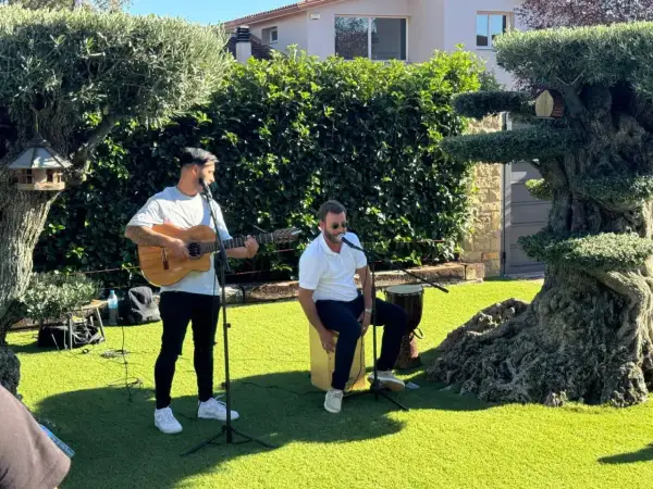 Dos músicos animan el jardín con rumbas para bailar. Uno toca la guitarra y canta, el otro canta y percute un cajón.