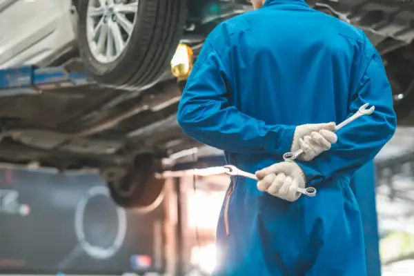 Meccanico in tuta blu con chiavi inglesi, pronto per i tagliandi auto. L'auto è sollevata sul ponte.