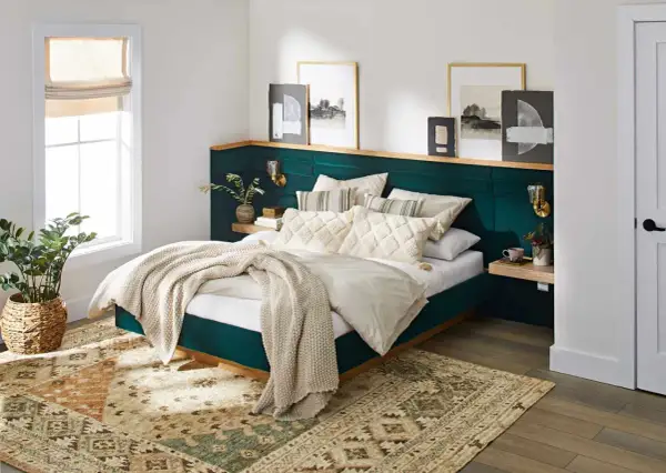 A plush, emerald green headboard with a wooden shelf above offers unique headboard ideas. Artwork and sconces adorn the wall.
