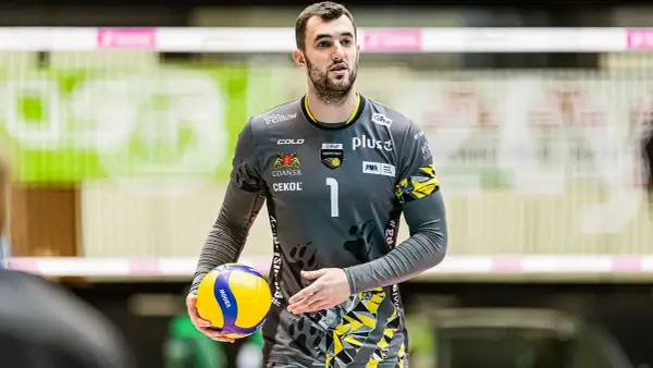 Bartłomiej Lipiński, siatkarz w szarym stroju z numerem 1, trzyma piłkę do siatkówki.