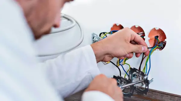 Elektryk dokonuje wymiany instalacji elektrycznej, podłączając przewody do puszek.