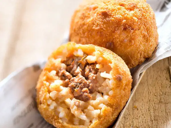 Deux arancini bolognaise dorés et croustillants, l'un ouvert révélant un cœur de riz et de viande savoureux.