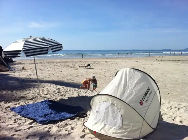 Na plaży rozłożony namiot i koc, idealne miejsce, by sprawdzić, czy można spać na plaży. Dzieci bawią się w piasku, a w tle widać morze.