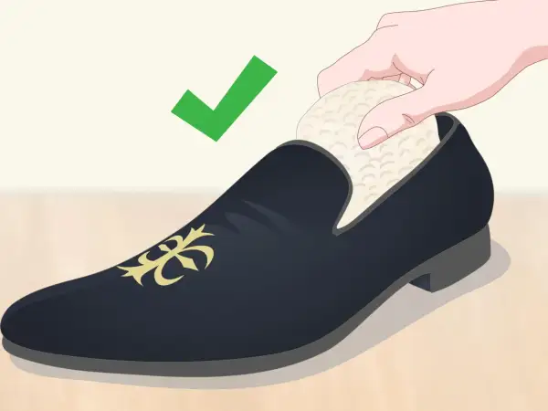 Une main insère un embauchoir dans une chaussure de ville noire ornée d'un motif doré. La mise en forme des chaussures est essentielle pour leur longévité. ✅