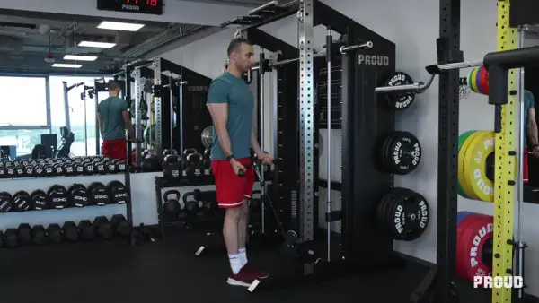 Mężczyzna wykonuje ćwiczenia na biceps przy użyciu wyciągu. W tle widoczne są sztangi, hantle i talerze obciążeniowe.