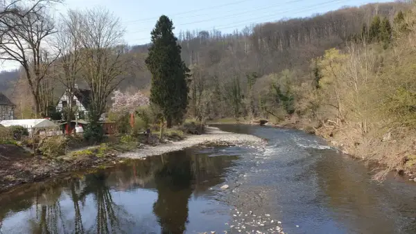 Idyllische Flusslandschaft am Wupperhof Solingen mit Fachwerkhäusern und bewaldeten Hängen.