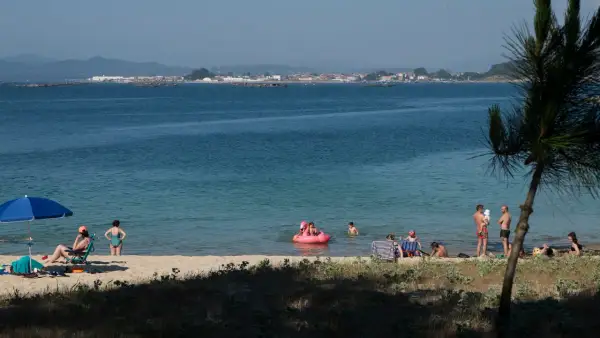 Gente disfruta de un día soleado en las playas de O Grove, con niños jugando en el agua y adultos relajándose en la arena.