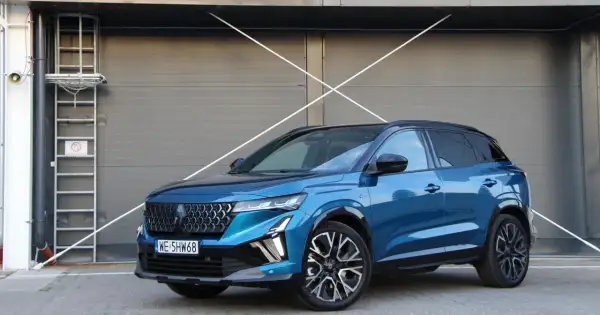 Błękitny Renault Austral 2025 z czarnym dachem i felgami stoi przed szarą, nowoczesną bramą.