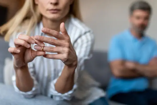 Kobieta zdejmuje obrączkę, symbol końca małżeństwa. W tle siedzi mężczyzna. Wzór pozwu o rozwód z orzeczeniem o winie męża.