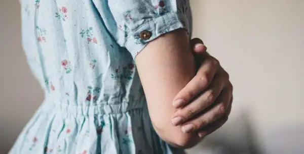 Een vrouw in een bloemenjurk houdt haar arm vast, misschien om oefeningen tegen trillende handen te doen.