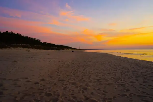 Piękny zachód słońca nad morzem. Niebo mieni się odcieniami różu i pomarańczy, a plaża jest pusta, tylko ślady stóp przypominają o minionych spacerach.