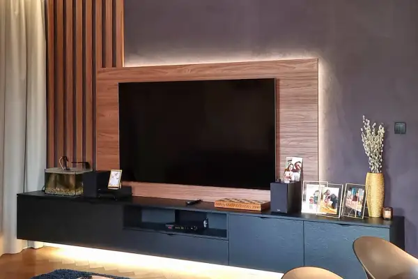 Nowoczesny salon z telewizorem w zabudowie meblowej. Drewniane panele i subtelne podświetlenie tworzą przytulną atmosferę.