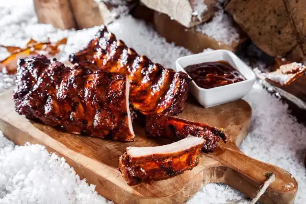 Saftige spareribs im backofen, glasiert und mit BBQ-Sauce, auf einem Holzbrett mit Schnee dekoriert.