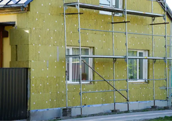 Lavori in corso per pulire muro esterno con cappotto isolante. L'edificio è circondato da ponteggi metallici.