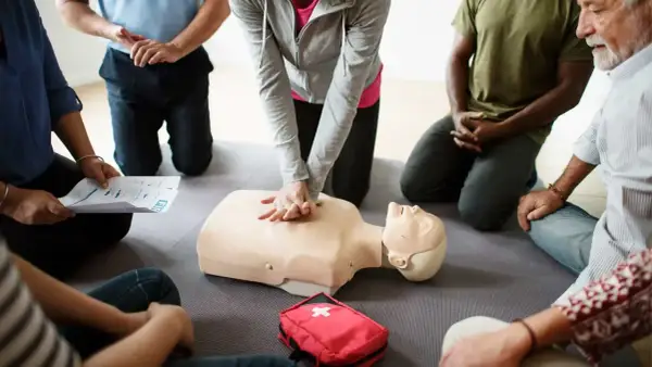 Persone in cerchio praticano RCP su un manichino. Si impara da chi sono designati gli addetti al primo soccorso.