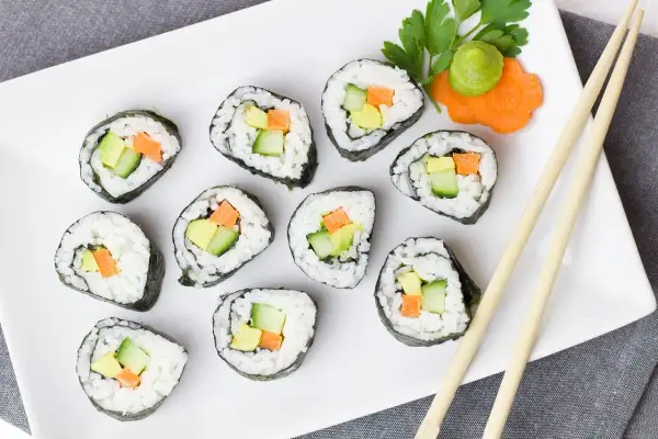 Zestaw do robienia sushi w domu: świeże rolki z awokado, ogórkiem i marchewką, podane z wasabi i pałeczkami.