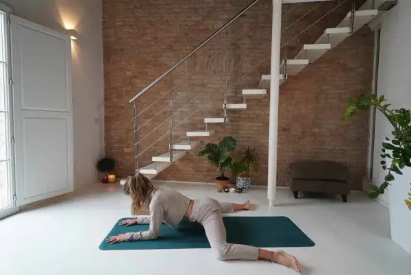 Donna in posizione rana yoga, con le ginocchia divaricate e il busto appoggiato sugli avambracci.