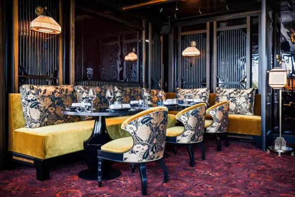 Ambiance luxueuse d'un restaurant à mun paris. Banquettes velours ocre, coussins fleuris, chaises élégantes et tapis persan.
