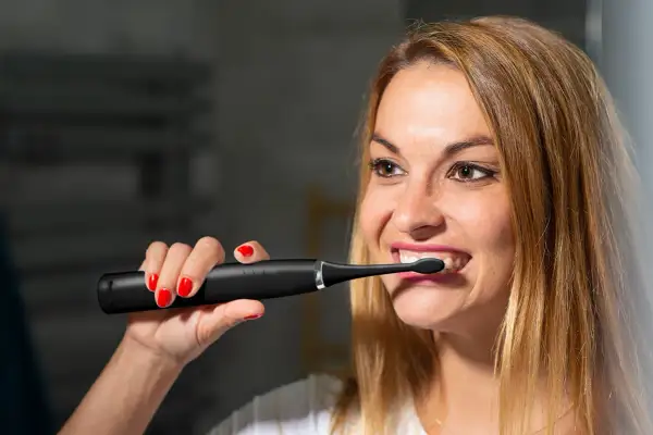 Kobieta z czerwonymi paznokciami używa czarnej szczoteczki sonicznej do zębów.