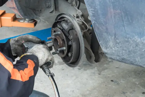 Mécanicien travaillant sur un tambour de frein usé. L'outil pneumatique est utilisé pour retirer les boulons de la roue.