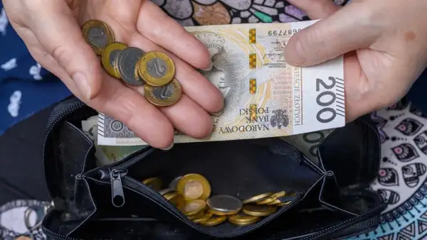Dłonie trzymające polskie banknoty i monety nad otwartym portfelem.