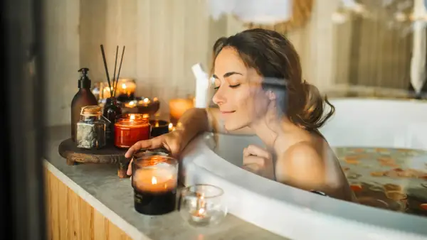 Entspannter beauty day zuhause: Frau genießt ein warmes Bad mit Kerzenlicht und duftenden Ölen.