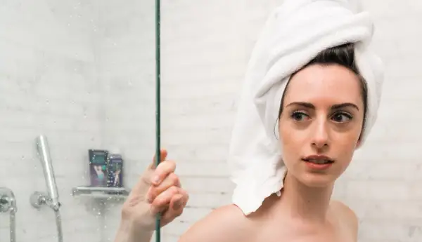 Ragazza con asciugamano in testa guarda preoccupata la doccia, pensando che la paraffina liquida fa male alla pelle.