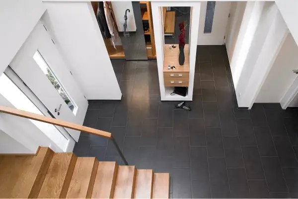 Moderner Flur nach Renovierung: Holzboden, dunkle Fliesen, Garderobe mit Spiegel und Blumen.
