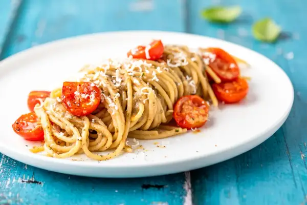 Spaghetti conditi con una cremosa salsa alle melanzane, guarniti con pomodorini confit e parmigiano grattugiato.