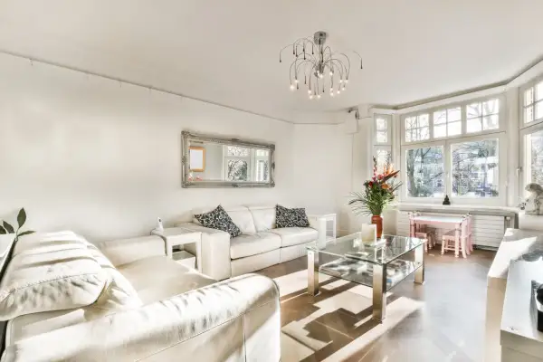 Jasny salon z białymi sofami, szklanym stolikiem i ozdobnym lustrem. Inspiracje salonem w stylu francuskim.