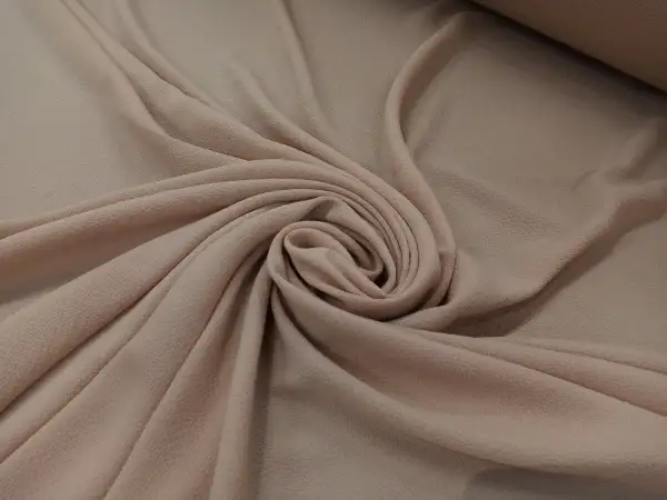 Delikatna, beżowa żorżeta układa się w miękkie fałdy, tworząc elegancką spiralę.