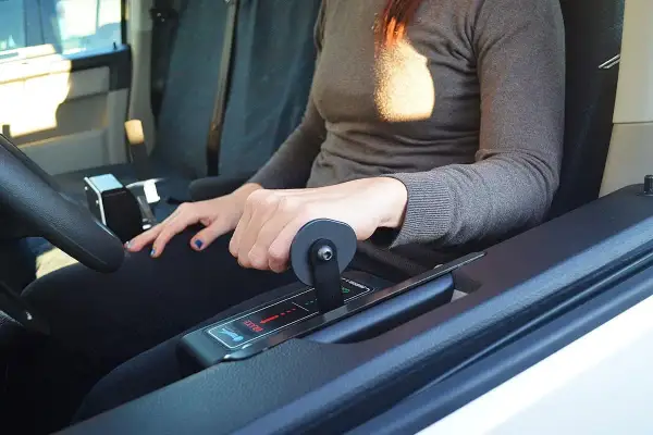Mano che aziona la leva di un allestimento auto per disabili, con indicazioni "brake" e frecce.