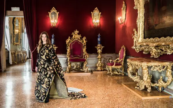 Donna con abito prezioso in una sala dorata, un'elegante tessitura Bevilacqua per una visita regale.