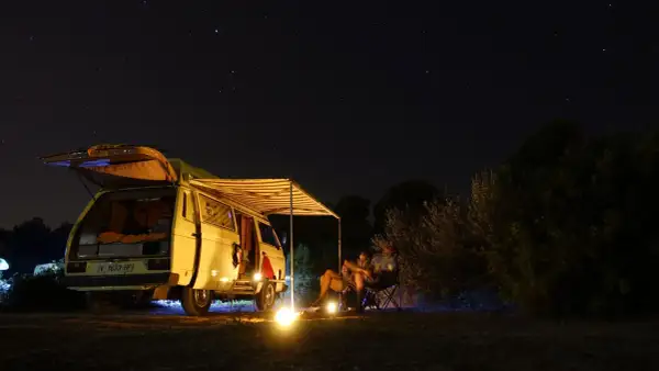 Sternenhimmel über einem Campervan mit ausgefahrener Markise. Ein Paar sitzt davor, die perfekte Mallorca Route für Camper.