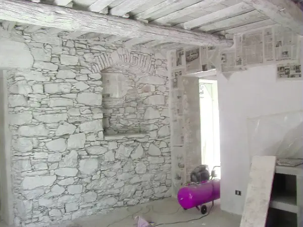 Interno con muro in pietra e intonaco grezzo, travi a vista e un compressore rosa.