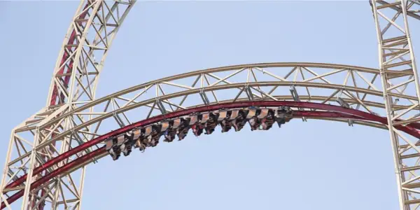 Wagoniki rollercoaster w Polsce pędzą po czerwonym torze na tle błękitnego nieba.