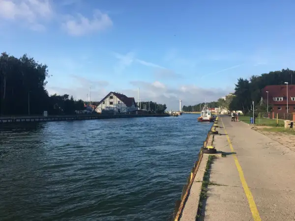 Spacerem nad jeziorem Sarbsko, widać kanał, budynki i łodzie.