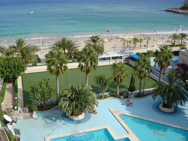 Vista aérea de un resort con piscina, cancha de césped, palmeras y una playa con el mar azul. Un lugar perfecto para sol y mar spa.