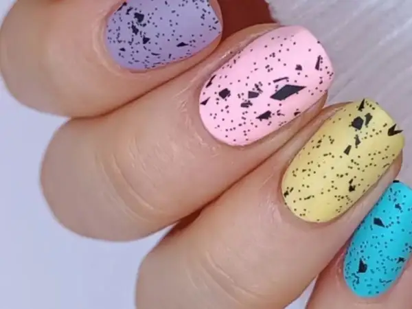 Delikatne, **milky nails** w pastelowych kolorach: fioletowym, różowym, żółtym i turkusowym, ozdobione czarnymi plamkami imitującymi skorupki jajek.