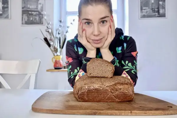 Kobieta zastanawia się, jaki chleb na odchudzanie wybrać. Na desce leżą dwa bochenki ciemnego pieczywa.