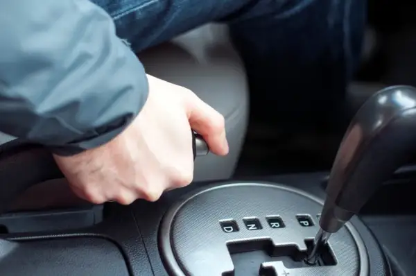 Main d'un conducteur actionnant le frein à main dans une voiture, prêt à démarrer.