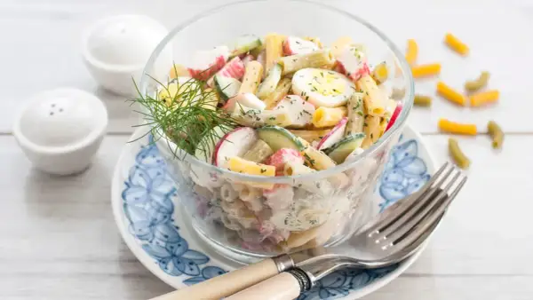 Salade de pâtes au surimi, œufs durs, concombre et radis, garnie d'aneth. Un délice frais et coloré.