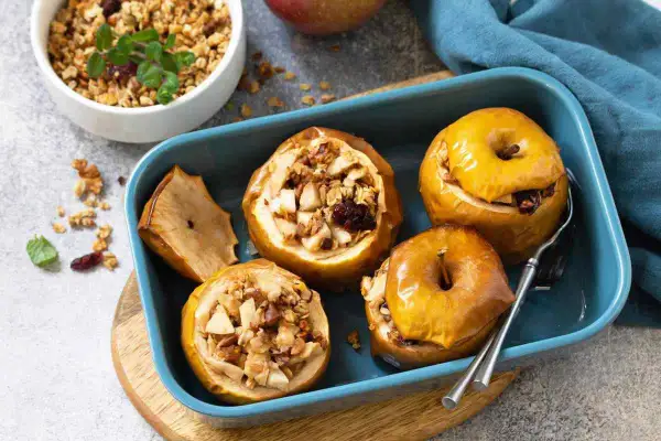 Mele cotte ripiene di frutta secca e granola, servite in una teglia blu.
